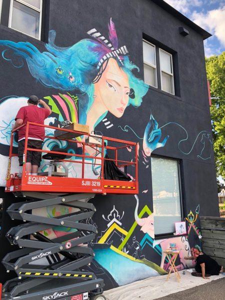 Mural artist Kao Lee Thao (lower right) is assisted by artist Ash
Kubesh as they complete “Our Common Threads” on the east wall
of Podiumwear, 2408 W. Territorial Rd. Photo by Mindy Keskinen