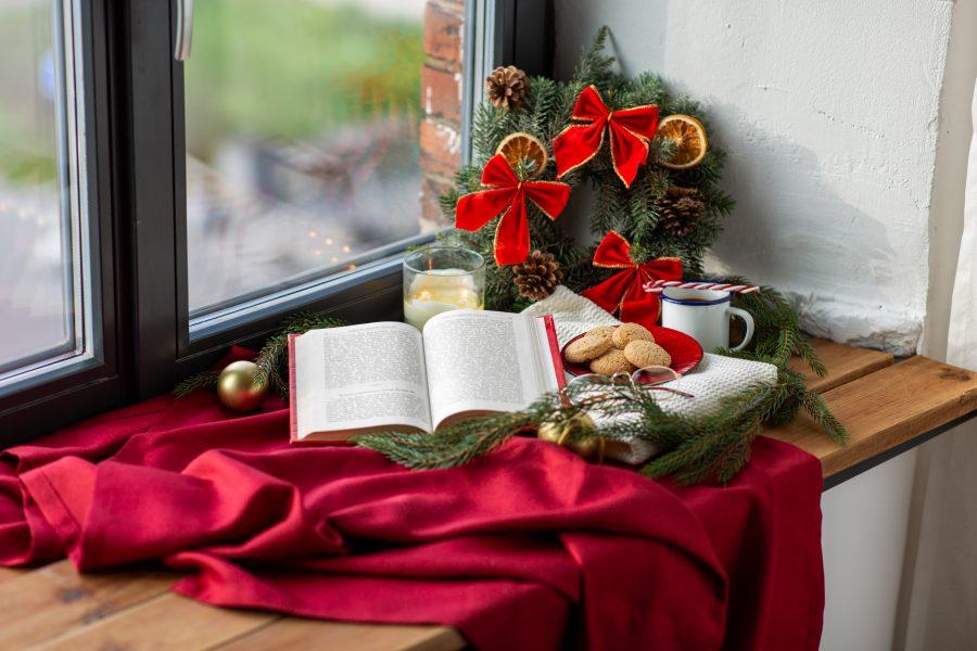 winter holidays and leisure concept - open book, fir branch, oatmeal cookies, coffee and christmas decorations on window sill at home